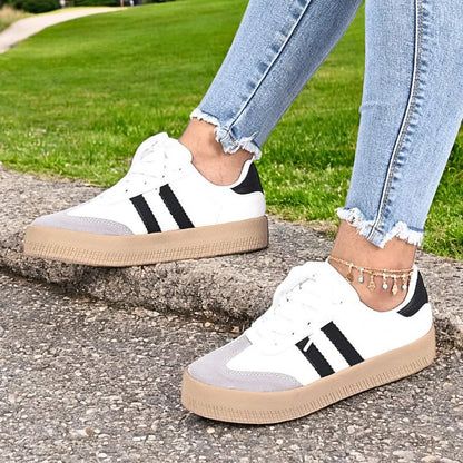 Modelo femenino posando con Zapatilla Suelaviva Vento en blanco desde la rodilla hacia abajo, diseño clásico y deportivo con puntera texturizada tipo gamuza, suela de goma beige, detalles de cuero sintético, perfecta para outfits casuales y versátiles.